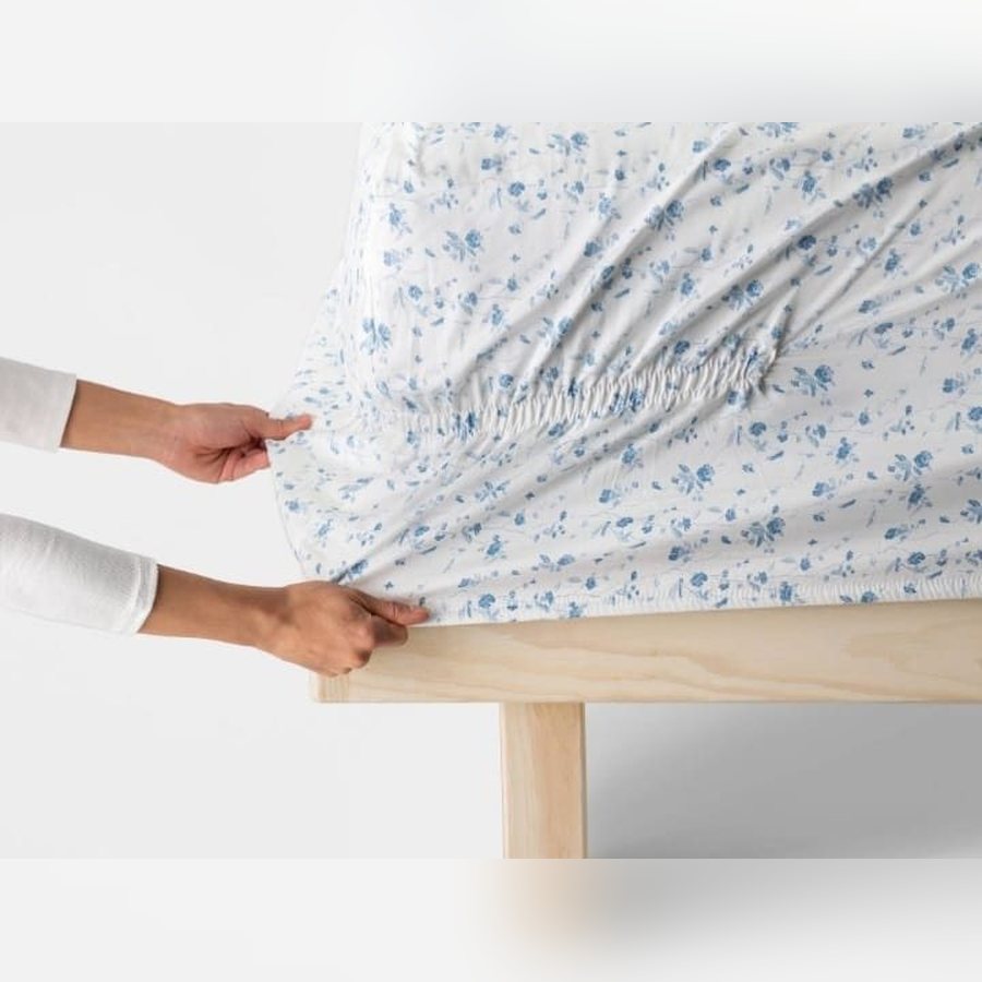 White sheet with a blue floral print fitted on a bed